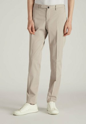 Pantaloni beige chiaro in tessuto morbido, con taglio dritto, piega frontale e vita con chiusura a bottone. Abbinati a sneakers bianche.