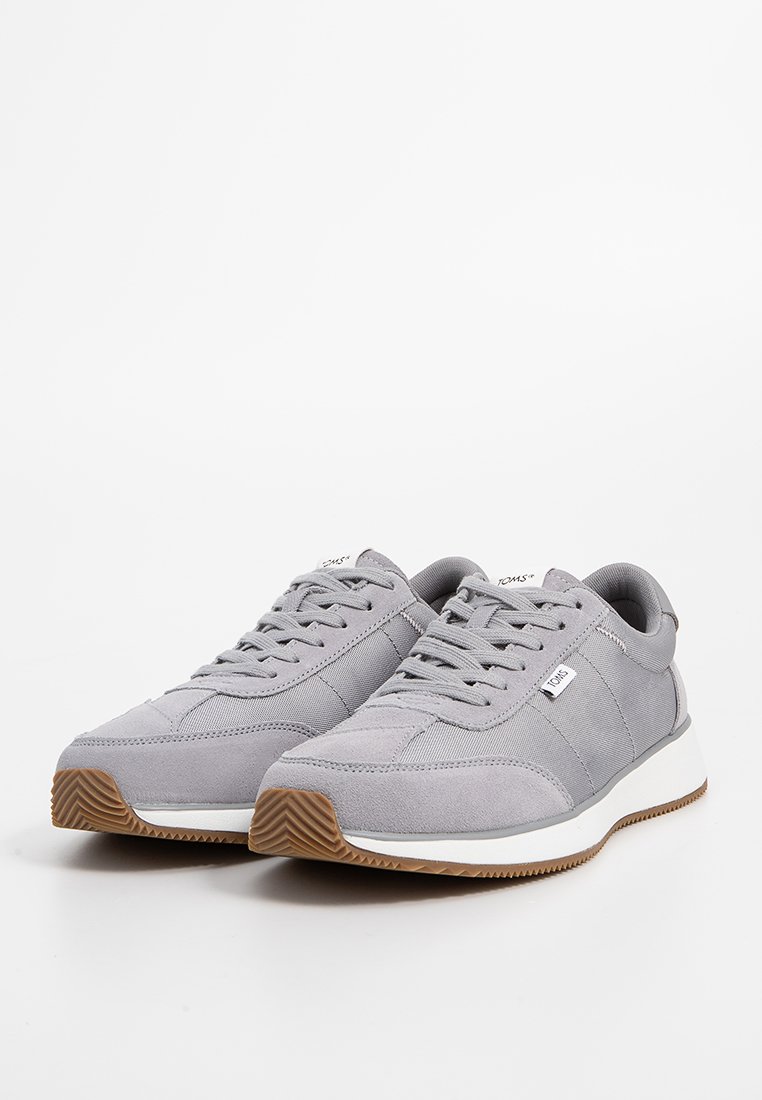 Baskets gris clair présentant un mélange de matériaux lisses et texturés, un design à lacets, une semelle en caoutchouc avec un motif de grip marron et un détail de logo.