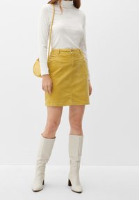 Gul kordflöjlskjol med en slät yta, med längd till mitten av låret, framfickor och knappstängning, kombinerad med vita knälånga stövlar.