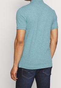 Polo bleu clair à manches courtes, doté d'un col classique et d'ouvertures latérales. Porté avec un jean denim foncé.