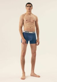 Męskie granatowe bokserki z białym elastycznym pasem z nadrukiem "HENDERSON". Materiał wydaje się gładki i dopasowany. Model stoi na boso.