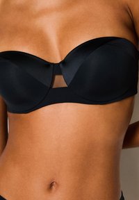 Reggiseno nero senza spalline realizzato in satin liscio con una silhouette strutturata, caratterizzato da un pannello in rete al centro. Il design è senza cuciture e privo di decorazioni.