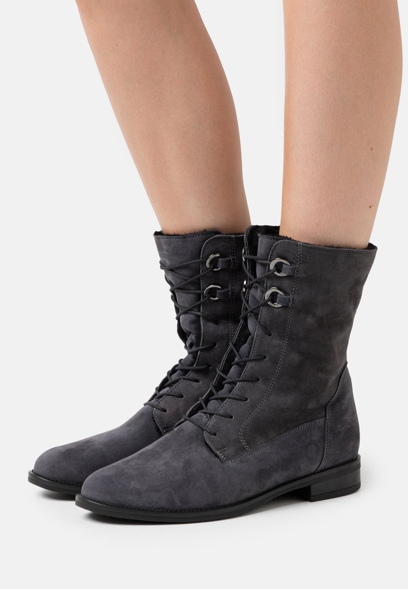 Bottes cheville en daim gris avec un bout arrondi, une fermeture à lacets à l'avant et des œillets métalliques. Semelle plate et texture douce.