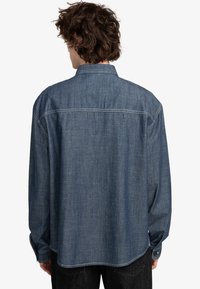 Jeansskjorte i mørkeblå, med en afslappet pasform, lange ærmer, knapmanchetter og kontrastsy, der løber langs sømmene og ryggen.