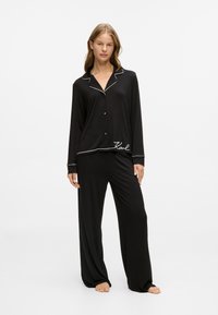 Črno pižamo s dolgimi rokavi in hlačami. Ima belo obrobo na ovratniku in manšetam ter vezenje "Karl" na robu. Mehka tkanina.