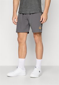 Gray athletic shorts with an elastic waistband and side pockets. Features a small logo in orange. Paired with white sneakers and socks.