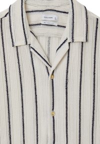 Chemise légère de couleur crème avec des rayures verticales bleu marine, fermeture à boutons et coupe décontractée. Tissu texturé avec un col classique.
