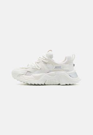 Maswny biały sneaker z teksturowaną podeszwą, panelami z siateczki, grubymi sznurowadłami oraz pętelką na pięcie, pokazany z boku na jednolitym tle.