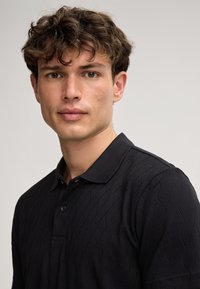 Schwarzes Poloshirt mit strukturierter Rautenoptik, kurzen Ärmeln und einer Knopfleiste mit drei Knöpfen. Mit Kragen und glatter Oberfläche.