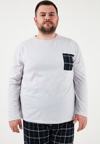 Pikad varrukad hall särk pehmest materjalist, millel on tumesinine ruuduline tasku, koos musta ja valge ruudulise pükstega.