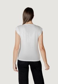 T-shirt bianca a maniche corte con scollatura tonda e texture liscia, indossata con pantaloni neri, che presenta un design semplice e pulito.