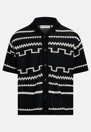 Chemise noire à manches courtes avec boutons, motifs géométriques blancs et col, texture en tricot, étiquette "Redefined Rebel" à l'intérieur du col.