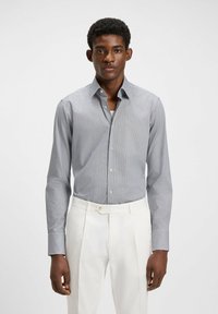 Randig skjortklänning i blått och vitt, knäppning fram med krage, lång ärm, textil med struktur. Matchas med ljusa byxor.