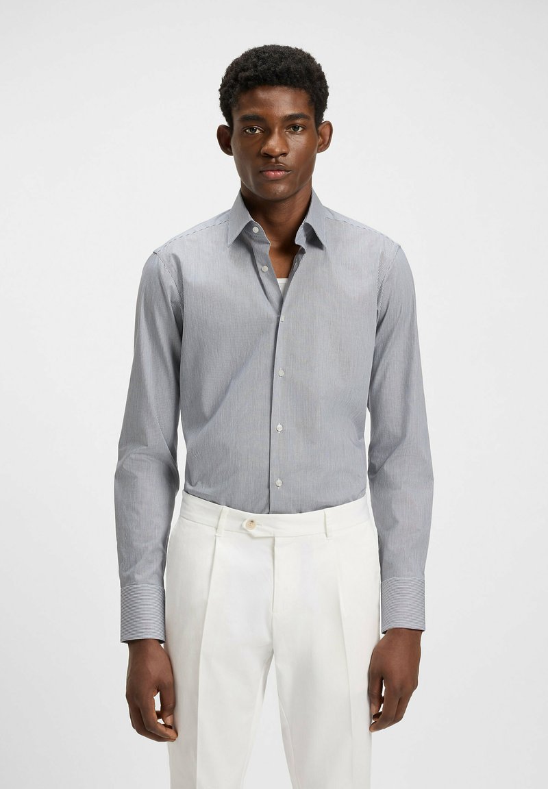 Randig skjortklänning i blått och vitt, knäppning fram med krage, lång ärm, textil med struktur. Matchas med ljusa byxor.