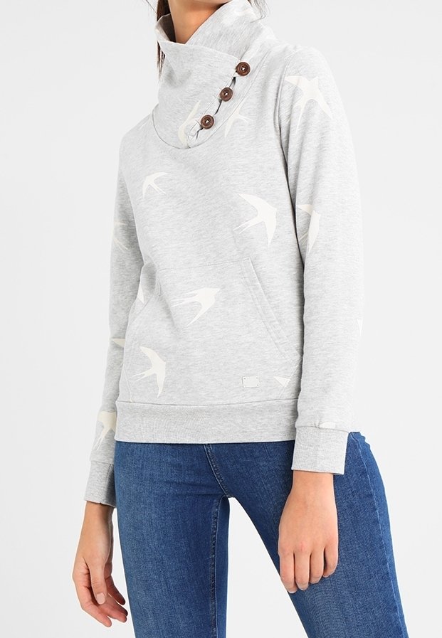 Sweat-shirt gris clair avec motifs d'oiseaux blancs, col montant asymétrique avec boutons, poche kangourou, porté avec un jean bleu.