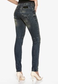 Dunkelblaue Skinny Jeans aus Denim mit einem ausgewaschenen Finish, ausgestattet mit mehreren Gesäßtaschen und kontrastierenden Nähten, kombiniert mit High Heels.