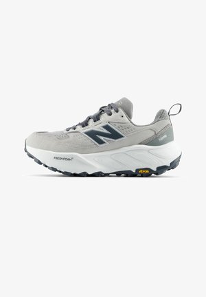 Grijze en witte New Balance sportschoen met zwarte zool, Fresh Foam demping, Vibram buitenzool en trek-lipje aan de hiel.