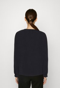 Granatowa bluzka z długim rękawem, wykonana z teksturowanej tkaniny, z okrągłym dekoltem. Posiada zapinane mankiety i luźny krój, zaprojektowana z myślą o komforcie.