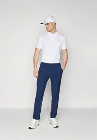 Fehér galléros póló, tengerészkék nadrág és fehér sportcipő. A sapka fehér, fekete logóval. Egyszerű dizájn, testhezálló szabás.