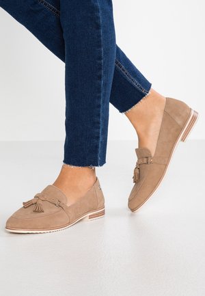 Beige loafers lavet af blødt ruskind med kvastdetaljer, en lav hæl og læderkant. Kombineret med mørkeblå denimjeans.