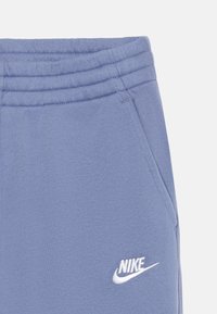 Calças de treino Nike de azul claro, feitas de um tecido macio com uma cintura canelada, apresentando bolsos laterais e um logotipo branco na coxa esquerda.