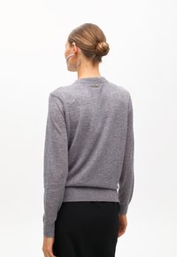 Jasnoszary sweter dzianinowy z okrągłym dekoltem, długimi rękawami i ściąganym dołem. Z tyłu znajduje się mały złoty akcent w kształcie litery "M".