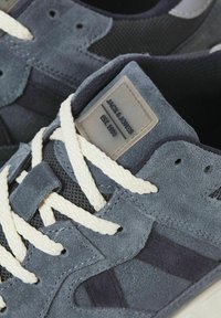 Mørkeblå ruskinds sneakers med mesh-detaljer, offwhite snørebånd og et mærketag. Har en tekstureret overflade og et afrundet tådesign.