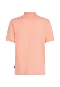 Polo à manches courtes de couleur pêche clair, fabriqué en tissu doux avec une texture lisse, doté d'un col classique et d'échancrures sur les côtés.