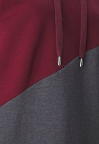 Sudadera en color burdeos y gris con un diseño de bloque de color diagonal, que cuenta con una tela suave, capucha y accesorios en plata en los cordones.