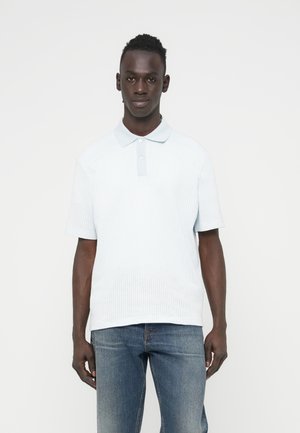 Lyseblå poloshirt med tekstureret mønster, korte ærmer og en tre-knaps stolpelukning. Kombineret med mediumvaskede denimjeans.