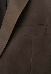 Gros plan d'une poche et d'un revers de veste de costume marron foncé avec des détails de coutures visibles sur un tissu lisse.