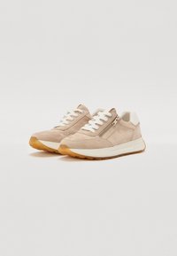 Baskets en suede beige clair avec lacets blancs, dotées d'une fermeture éclair sur le côté et d'une semelle en caoutchouc texturée pour une meilleure adhérence. Accentué par un tirant au talon blanc.