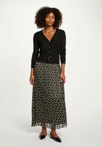 Zwart button-up cardigan met geribbelde textuur en lange mouwen, gecombineerd met een vloeiende, gestreepte maxi rok in zwart en goud.