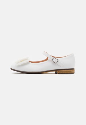 Chaussure Mary Jane blanche avec un petit talon, une boucle sur la bride de cheville et un nœud blanc décoratif sur le devant.