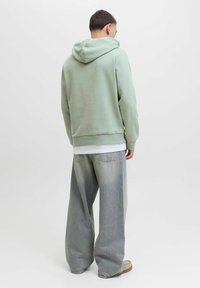 Lys grøn hættetrøje med kangaroo-lomme, parret med løstsiddende, falmede grå jeans. Har en afslappet pasform og blød tekstur.