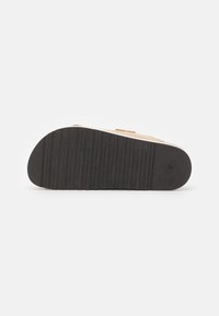 Brune ruskinds slip-on sandal med en flad sort gummisål, der har riller for bedre greb og en let opadgående kurve ved tåen.