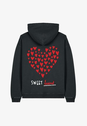 Melnā kapucēta džemperis ar lielu sirds dizainu, kas izveidota no sarkanām sirdīm un tekstu "SWEET heart" baltā un sarkanā krāsā.