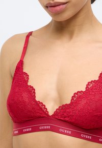 Rote Spitzen-Bralette mit gezacktem Rand und einem elastischen Band mit Markenlogo. Verfügt über verstellbare Träger und ein leichtes, strukturiertes Material.