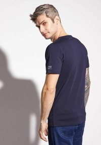 Granatowa bawełniana koszulka z krótkim rękawem i okrągłym dekoltem. Posiada małe logo na lewym rękawie. Prosty, klasyczny fason.