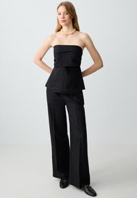 Zwarte linnen strapless top met gelaagd ontwerp, gecombineerd met wijde zwarte broek. Gladde textuur, geen patronen, minimale details.