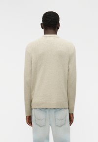 Ανοιχτό μπεζ πουλόβερ με υφασμάτινο πλεκτό σχέδιο, ριμπ μανσέτες και τελείωμα. Φορεμένο με ανοιχτό μπλε τζιν, αποπνέοντας casual, χαλαρή εφαρμογή.