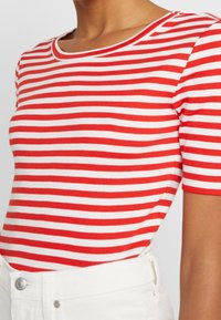Camiseta de manga corta a rayas rojas y blancas con escote redondo; fabricada en suave tejido de algodón; textura lisa y diseño ajustado.