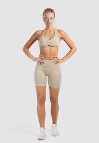 Beżowy prążkowany sportowy biustonosz z regulowanymi ramiączkami, w zestawie z dopasowanymi szortami z wysokim stanem, o gładkiej fakturze i obcisłym kroju.