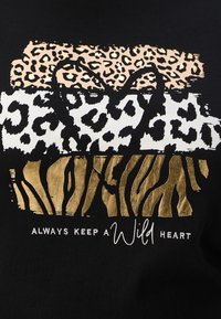 Juodas marškinėliai su leopardo ir zebro raštais auksinės, baltos ir smėlinės spalvos. Tekstas sako "Visada išlaikyk laukinį širdį" balta spalva.