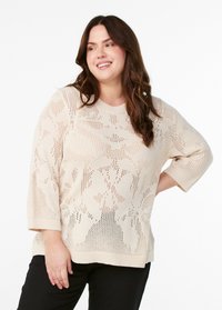 Pull en maille beige clair avec un motif texturé, des manches courtes et un col rond. Le design comprend des sections à tissage ouvert.