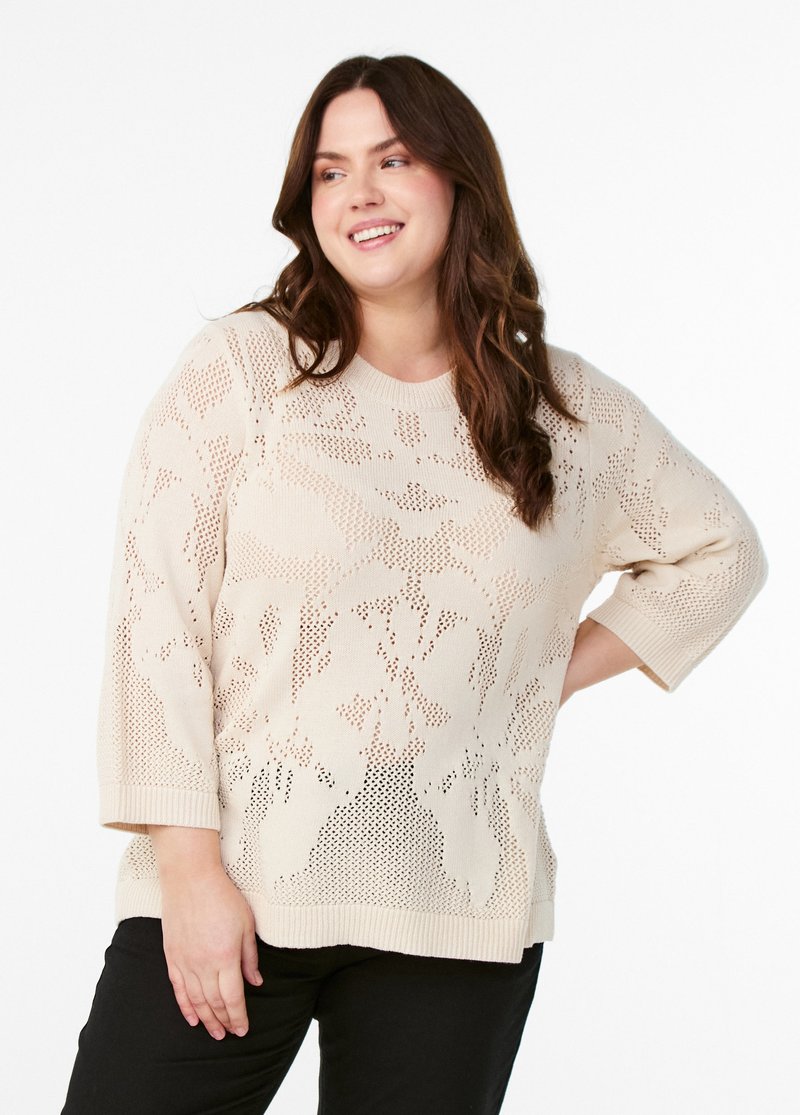 Pull en maille beige clair avec un motif texturé, des manches courtes et un col rond. Le design comprend des sections à tissage ouvert.