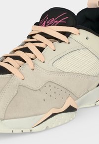 Μπεζ και μαύρο αθλητικό παπούτσι με ανοιχτορόζ κορδόνια, πλέγμα στην πλαϊνή επιφάνεια, σουέτ επιστρώσεις και τη λέξη «Flight» γραμμένη ροζ στη μαύρη γλώσσα.