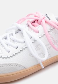 Prim-plan cu un sneaker alb din piele cu talpă gumă, având un șiret roz și unul alb, ambele legate, și detalii decorative cusute.