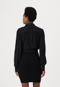 Blusa nera a maniche lunghe con dettaglio plissettato sul retro, abbinata a una mini gonna nera a costine. Entrambi i capi hanno una silhouette aderente.