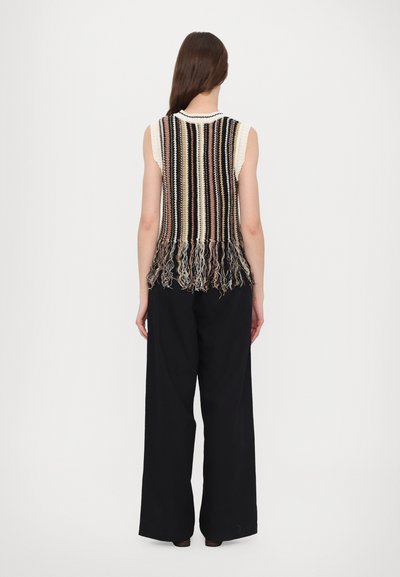 Stricktanktop ohne Ärmel mit vertikalen, mehrfarbigen Streifen und Fransenverzierung am Saum, kombiniert mit weit geschnittenen schwarzen Hosen.
